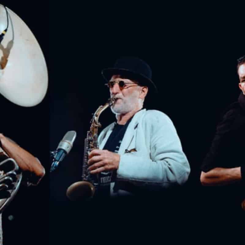 3 membres du groupe. Un avec un tuba, un avec un saxophone et un autre avec un accordéon.