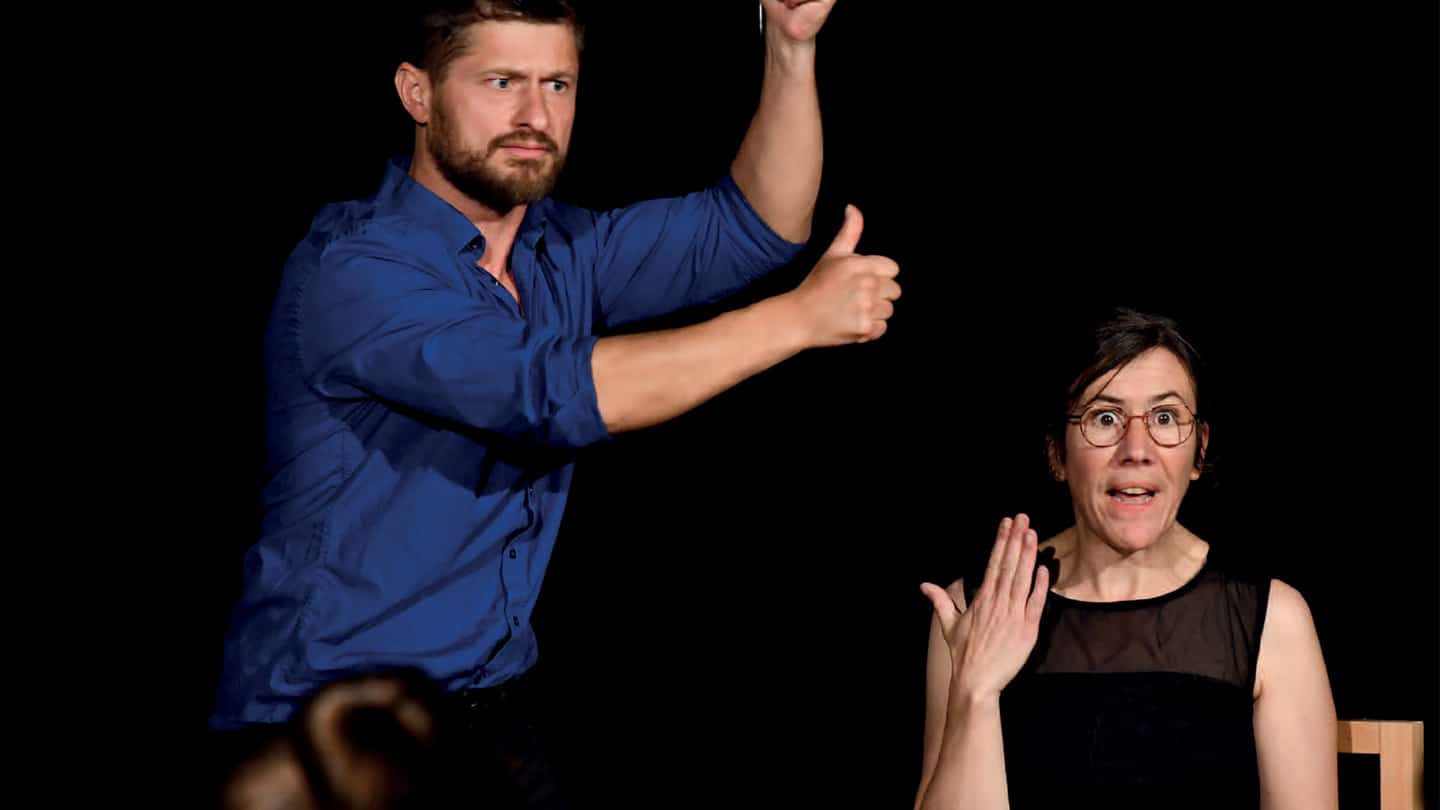 À droite, une comédienne semble surprise. À gauche, un comédien signe les bras levés.