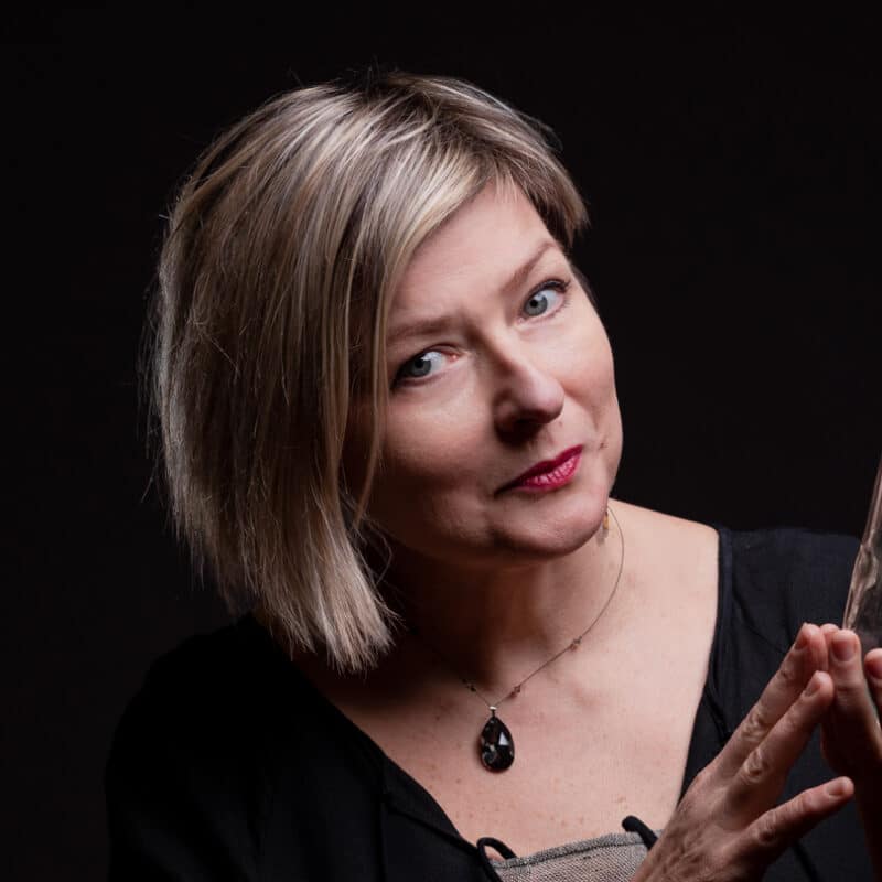 Portrait de la conteuse Magda Lena Gorska qui tient dans ses deux mains une longue fiole en verre