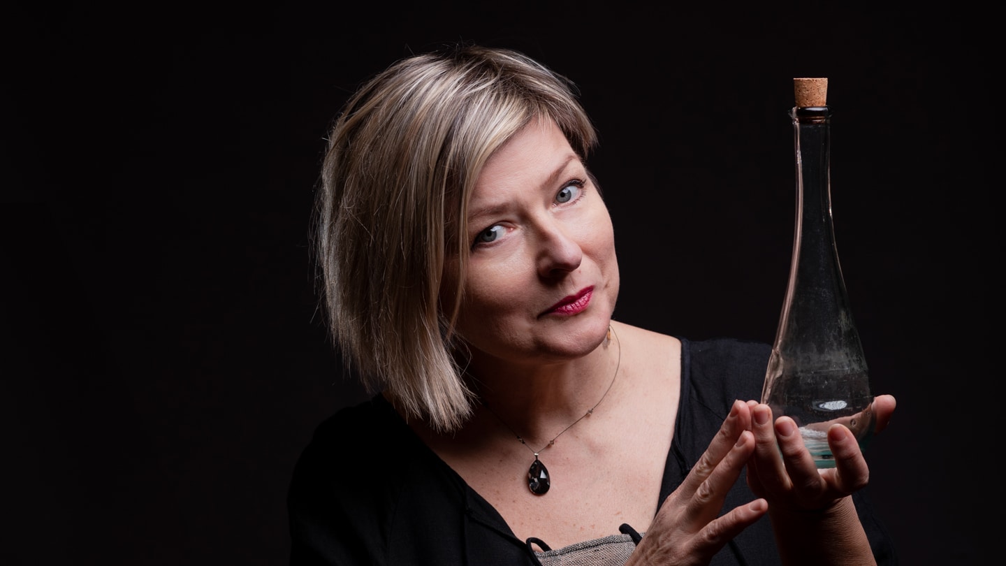 Portrait de la conteuse Magda Lena Gorska qui tient dans ses deux mains une longue fiole en verre