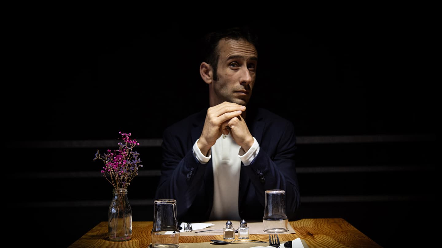 La table est mise pour 2 personnes, comme au restaurant. Un bouquet de fleurs séchées est gauche. Jérôme Pinel est assis à table et regarde en face de lui.