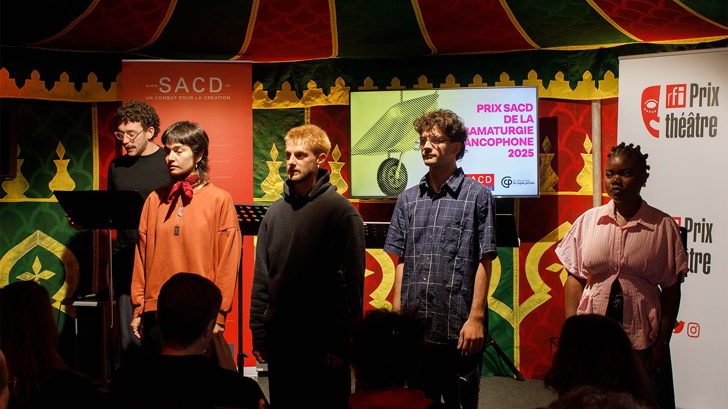 4 comédiens et comédiennes sont face aux publics. Un autre comédien, derrière un pupitre est en train de lire. En arrière plan, on lit Prix SACD de la dramaturgie francophone 2025.