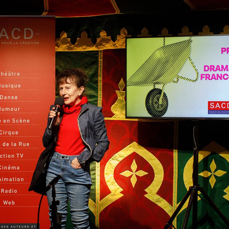Un femme parle dans un micro. Derrière elle on lit Prix SACD de la dramaturgie Francophone 2025.