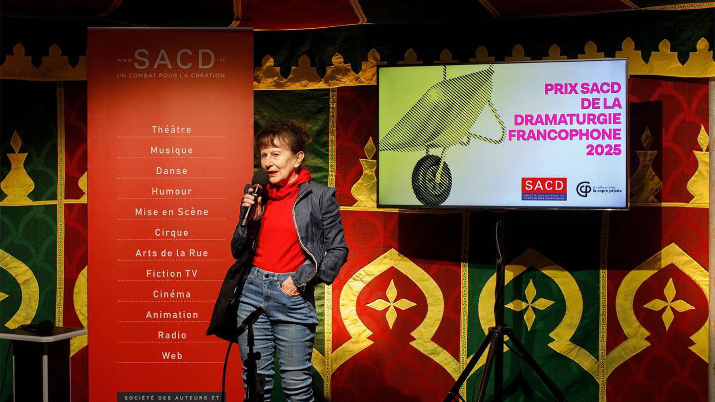 Un femme parle dans un micro. Derrière elle on lit Prix SACD de la dramaturgie Francophone 2025.