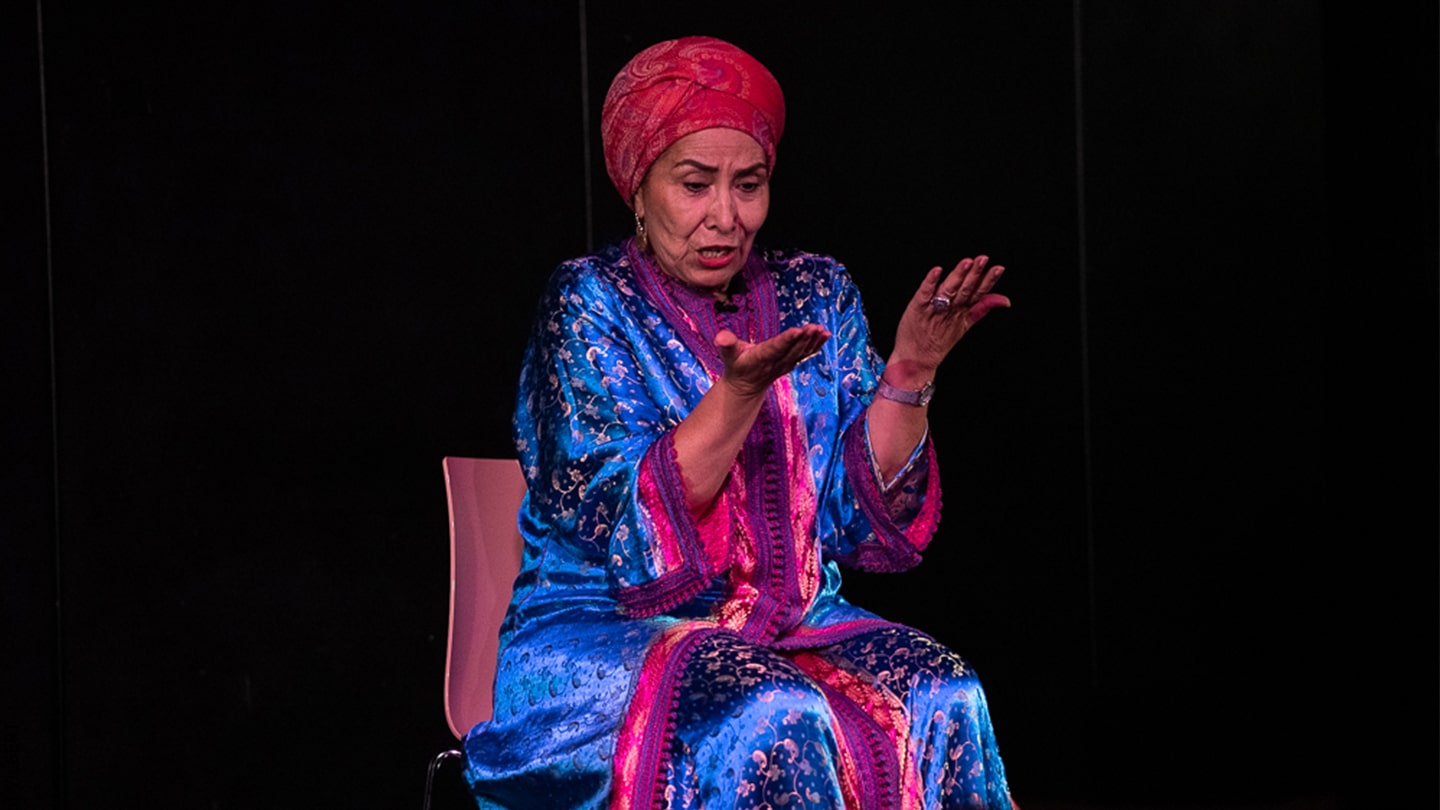 Halima Handame est au centre d'une scène en train de conter. Elle regarde ses mains.