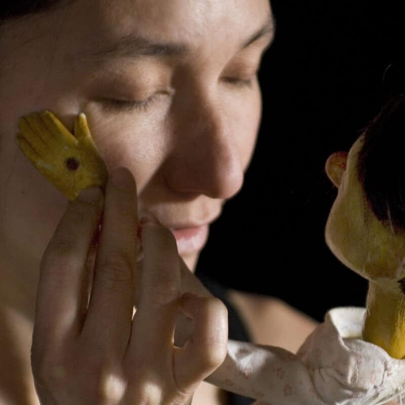 Une marionnette caresse la joue d'une femme. Elles se ressemblent.