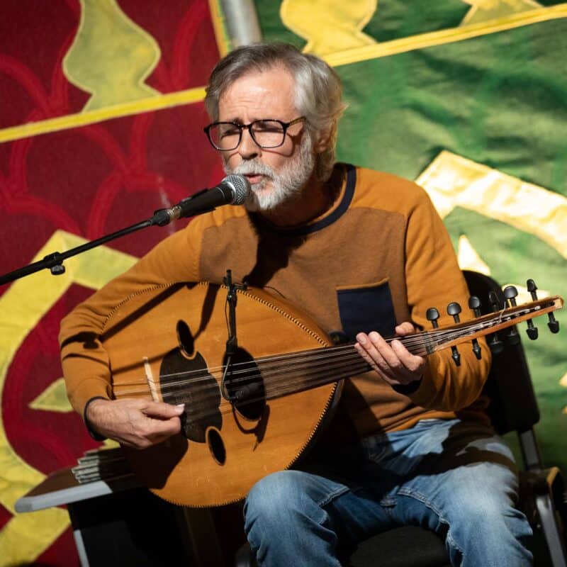 Photo d'Hassan Abd Alrahman, assis derrière un micro, en train de chanter les yeux fermés et de jouer du oud