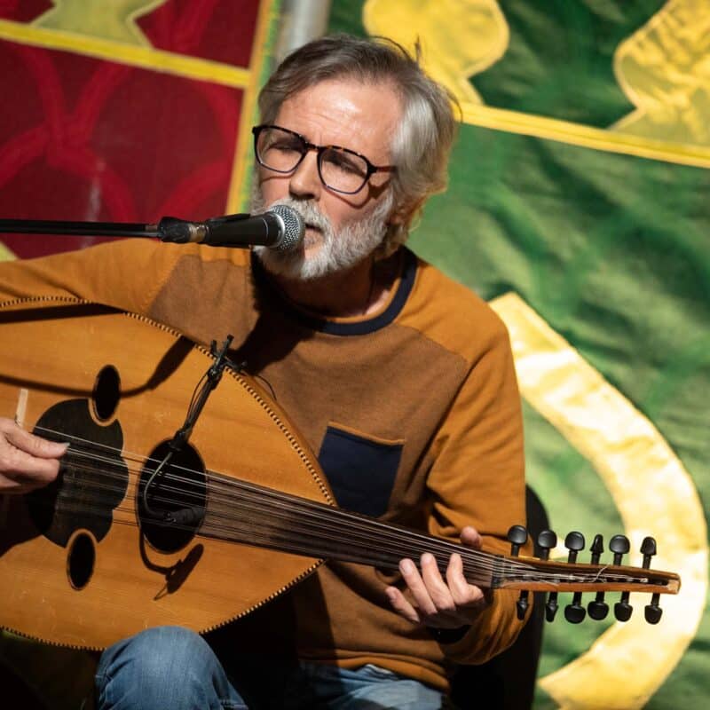 Photo d'Hassan Abd Alrahman, assis derrière un micro, en train de chanter les yeux fermés et de jouer du oud