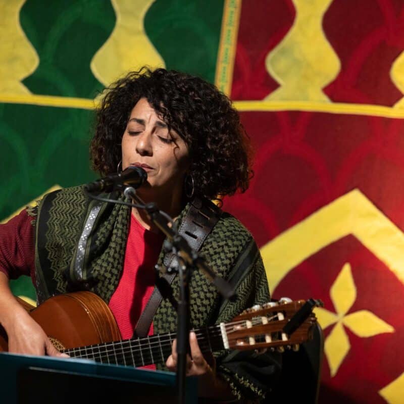 Photo de Chems Amrouche, assis derrière un micro, en train de chanter les yeux fermés et de jouer du oud