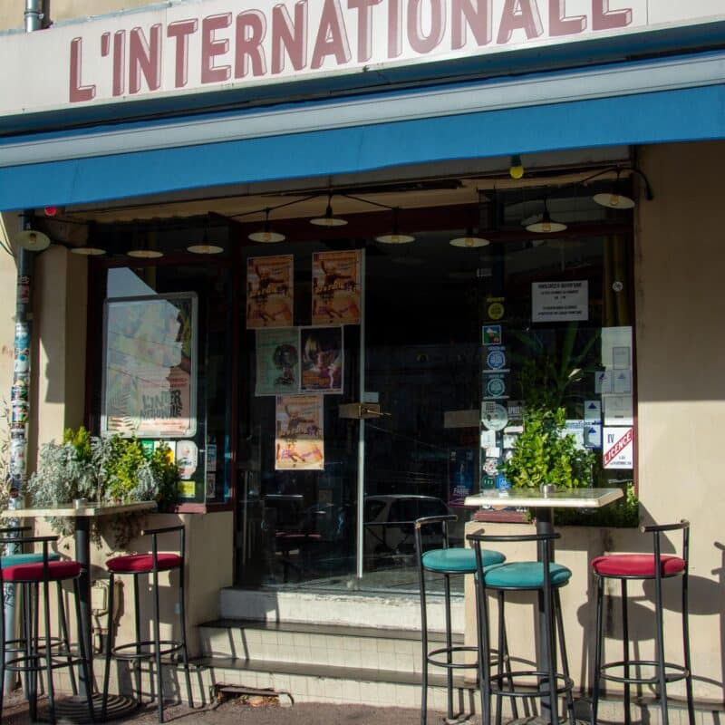 Vue de l'entrée et de la terrasse du bar restaurant L'Internationale avec quelques tabourets et tables hautes