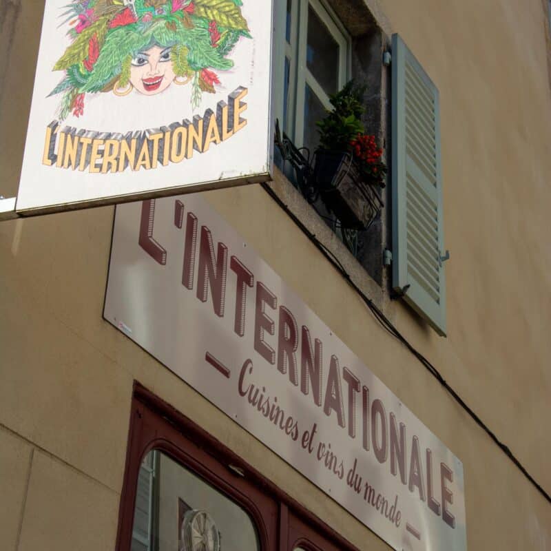 Enseigne du bar restaurant L'Internationale qui représente un dessin d'un visage de femme avec des cheveux en feuilles, fleurs, fruits, bouteilles de vins.