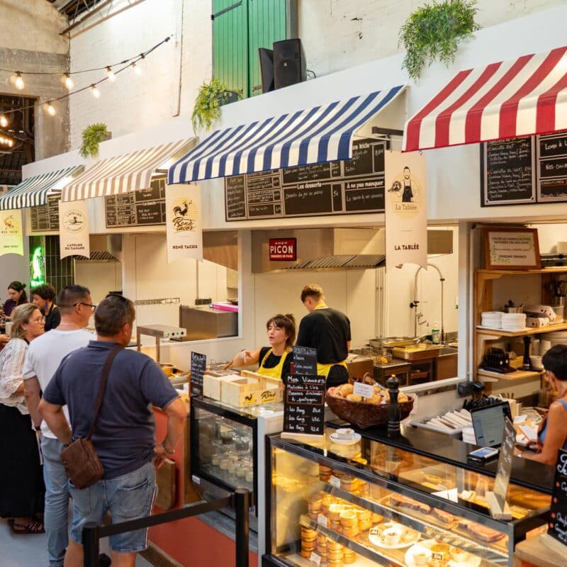 Photo des stands de nourriture à l'intérieur du marché des Jacobins et des personnes qui discutent avec les restaurateurices.