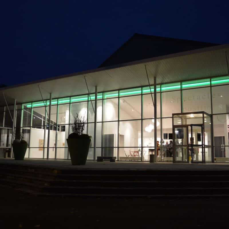Photo du parvis du centre culturel Jean-Pierre Fabrègue de nuit, avec des lumières à l'intérieur du bâtiment