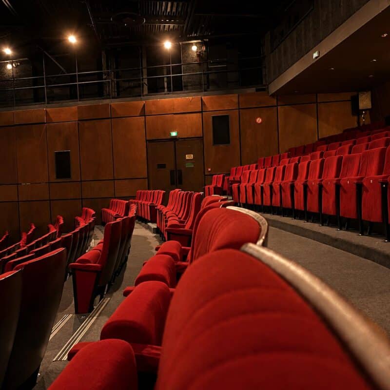 Photo de l'intérieur du théâtre depuis le milieu des gradins vers le côté de la salle et la sortie de secours