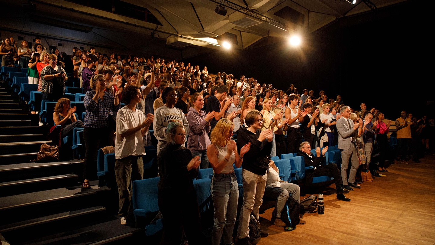 Dans une salle de spectacle, un public applaudit debout.
