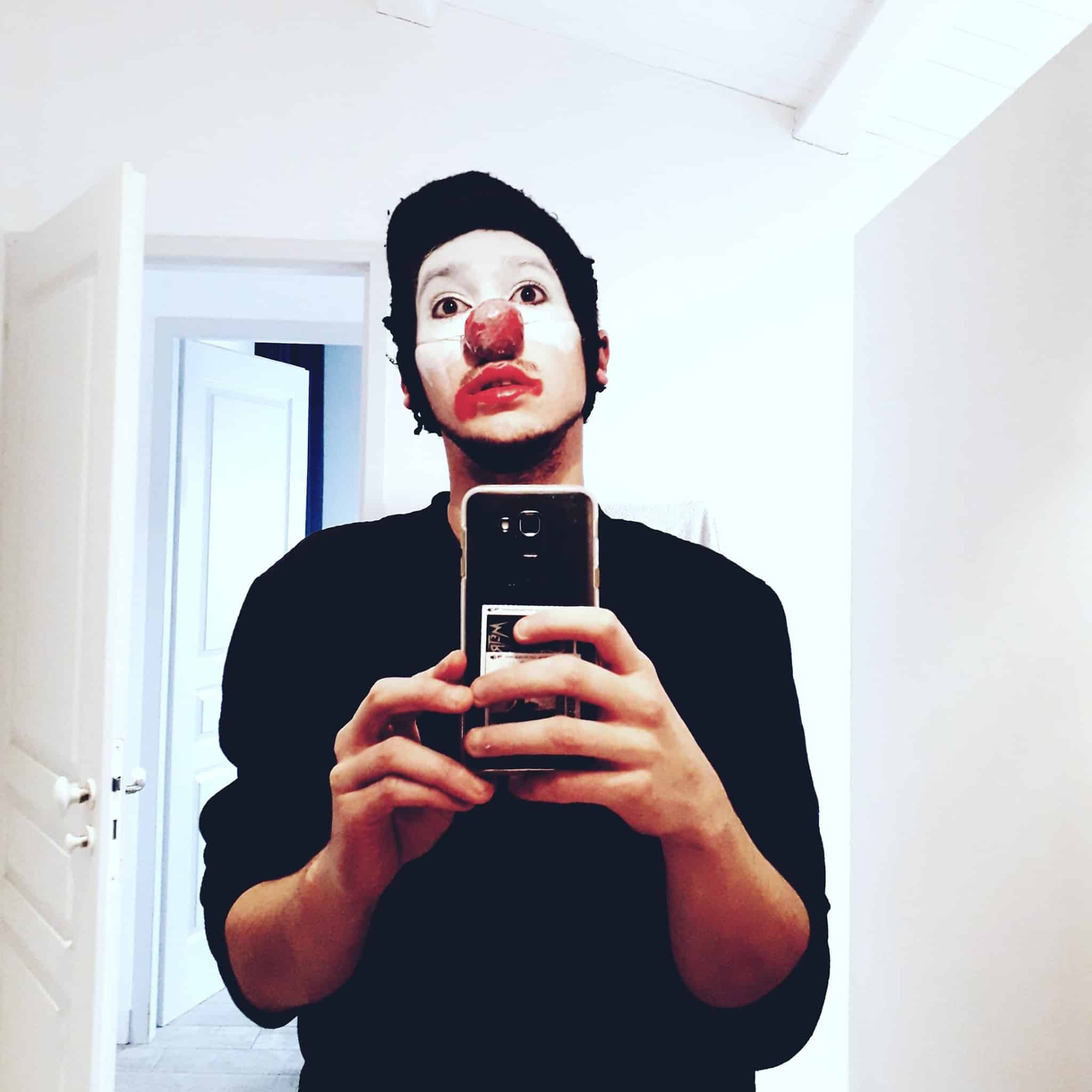 Autoportrait du clown de Clément Delpérié, au smartphone dans une pièce blanche, avec deux portes ouvertes derrière lui